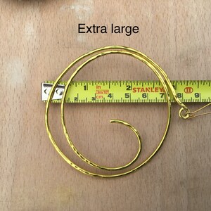 May include: Gold-toned metal hoop earrings with a spiral design. The earrings are 7 inches in diameter and have a hook closure.