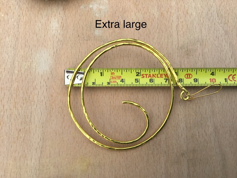 May include: Gold-toned metal hoop earrings with a spiral design. The earrings are 7 inches in diameter and have a hook closure.