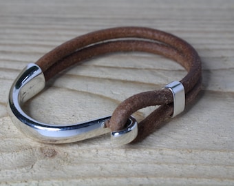 May include: A brown leather bracelet with a silver hook clasp. The bracelet is double-layered and has a simple design.