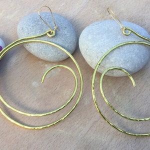May include: A pair of gold-toned hoop earrings with a spiral design. The earrings are made of hammered metal and have a simple, elegant look.