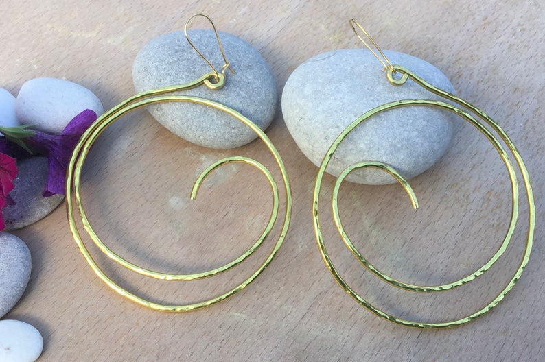 May include: A pair of gold-toned hoop earrings with a spiral design. The earrings are made of hammered metal and have a simple, elegant look.
