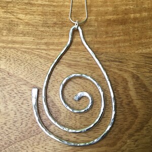May include: A silver pendant necklace with a hammered metal teardrop shape and a spiral design.