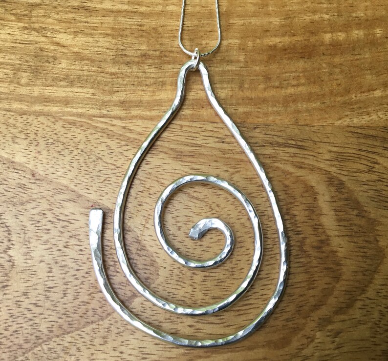 May include: A silver pendant necklace with a hammered metal teardrop shape and a spiral design.