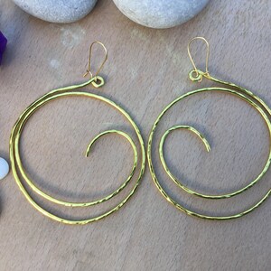 May include: A pair of gold-toned hoop earrings with a spiral design. The earrings are made of hammered metal and have a textured finish.
