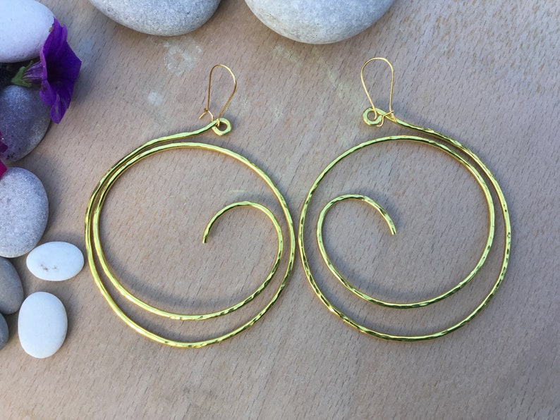 May include: A pair of gold-toned hoop earrings with a spiral design. The earrings are made of hammered metal and have a textured finish.