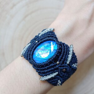 Peut inclure: Un bracelet en macramé bleu foncé avec une pierre précieuse irisée argentée et bleue au centre.