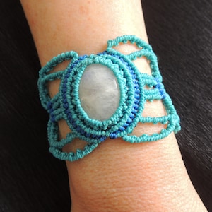 May include: A turquoise and blue macrame bracelet with a white oval gemstone in the center.