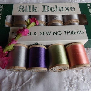 May include: A box of Belding Corticelli Silk Deluxe Sewing Thread. The box is green and white with the text "Silk Deluxe" and "Plus Silk Sewing Thread". There are four spools of thread in the image: silver, purple, green, and pink.