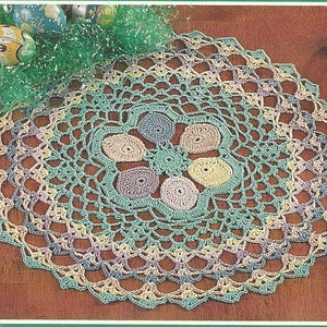 May include: A crocheted doily with a pastel green, yellow, and purple color scheme. The doily has a circular design with a center that resembles a flower.