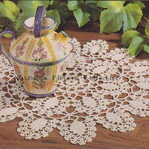 May include: A white crocheted doily with a scalloped edge and a floral design. A hand-painted ceramic pitcher with yellow, pink, and blue floral designs sits on top of the doily.