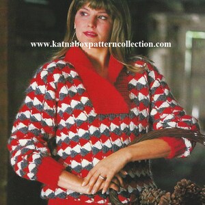 May include: A red, white, and gray knitted sweater with a geometric pattern. The sweater has a V-neck and long sleeves. The model is wearing a white skirt and holding a basket of pine cones.