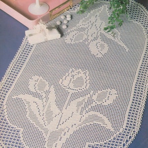 May include: A white crocheted oval table runner with a floral design. The runner features a delicate pattern of flowers and leaves, creating a beautiful and elegant centrepiece for any table.