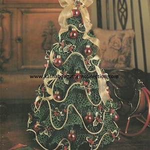 May include: A small artificial Christmas tree decorated with red ornaments, gold ribbon, and green holly sprigs. The tree is wrapped with a gold rope and sits on a wooden surface. The text "www.katnaboxpatterncollection.com" is visible at the bottom of the image.