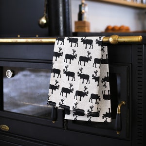 May include: A black cast iron wood-burning stove with a gold trim and a white tea towel with a black reindeer pattern hanging on a gold towel rack.