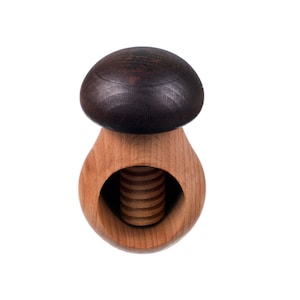May include: A wooden nutcracker shaped like a mushroom with a dark brown top and a light brown base. The nutcracker has a threaded screw in the center.