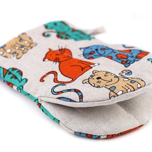 Pode incluir: Uma luva de forno bege com uma estampa de gato colorida. A luva apresenta uma variedade de gatos em diferentes cores e poses, incluindo laranja, azul e verde. A luva é feita de um tecido macio e durável e é perfeita para proteger suas mãos de superfícies quentes.