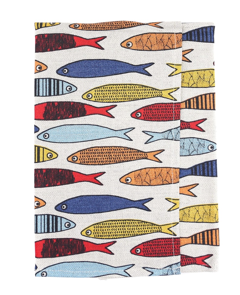 May include: A white fabric placemat with a colorful fish pattern. The fish are in various colors, including red, orange, yellow, blue, and black. The fish are all facing the same direction and have a simple, stylized design.