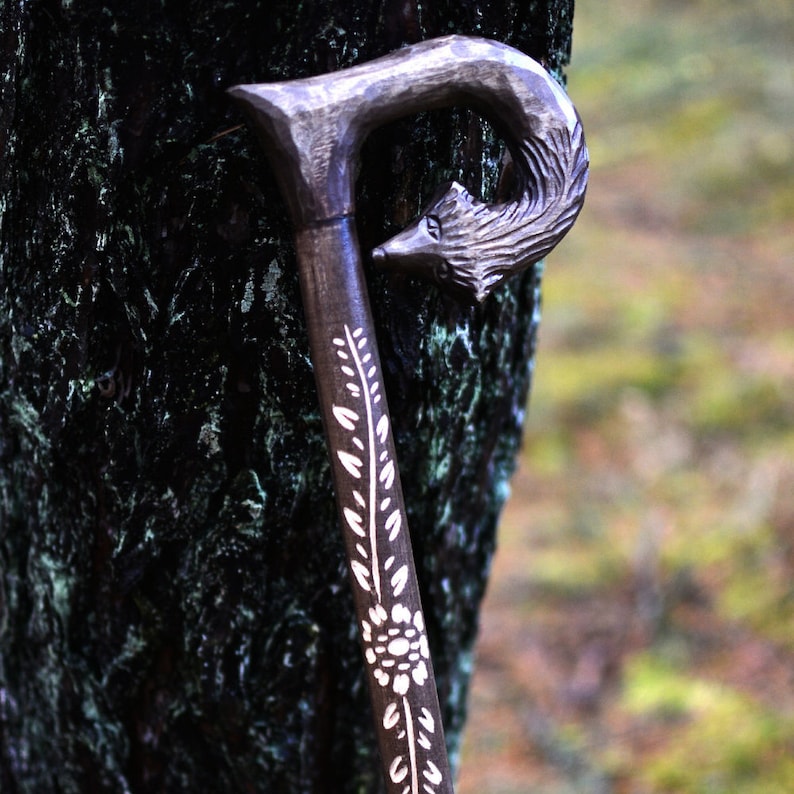 May include: A wooden walking stick with a carved wolf head handle and white floral designs. The stick is dark brown and the designs are white.