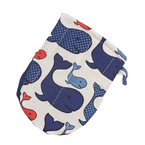 Pode incluir: Uma bolsa com cordão com um padrão repetido de baleias azul marinho e azul claro sobre um fundo creme. As baleias têm vários designs, incluindo bolinhas. Pequenos peixes vermelhos também estão espalhados pelo tecido.