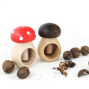 May include: Two wooden mushroom nutcrackers, one with a red and white cap and the other with a brown cap, with walnuts and walnut shells scattered around them.