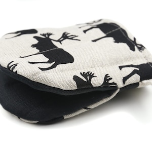 May include: A black and white oven mitt with a reindeer pattern. The mitt is made of a beige linen fabric with a black cotton lining.