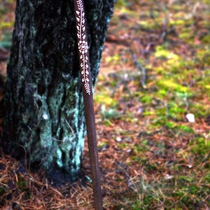 May include: A wooden walking stick with a carved bird head handle and floral design. The stick is brown and the carving is white.