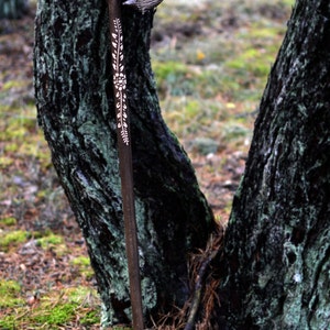 May include: A wooden walking stick with a carved, curved handle and a floral design. The stick is brown and the design is white.