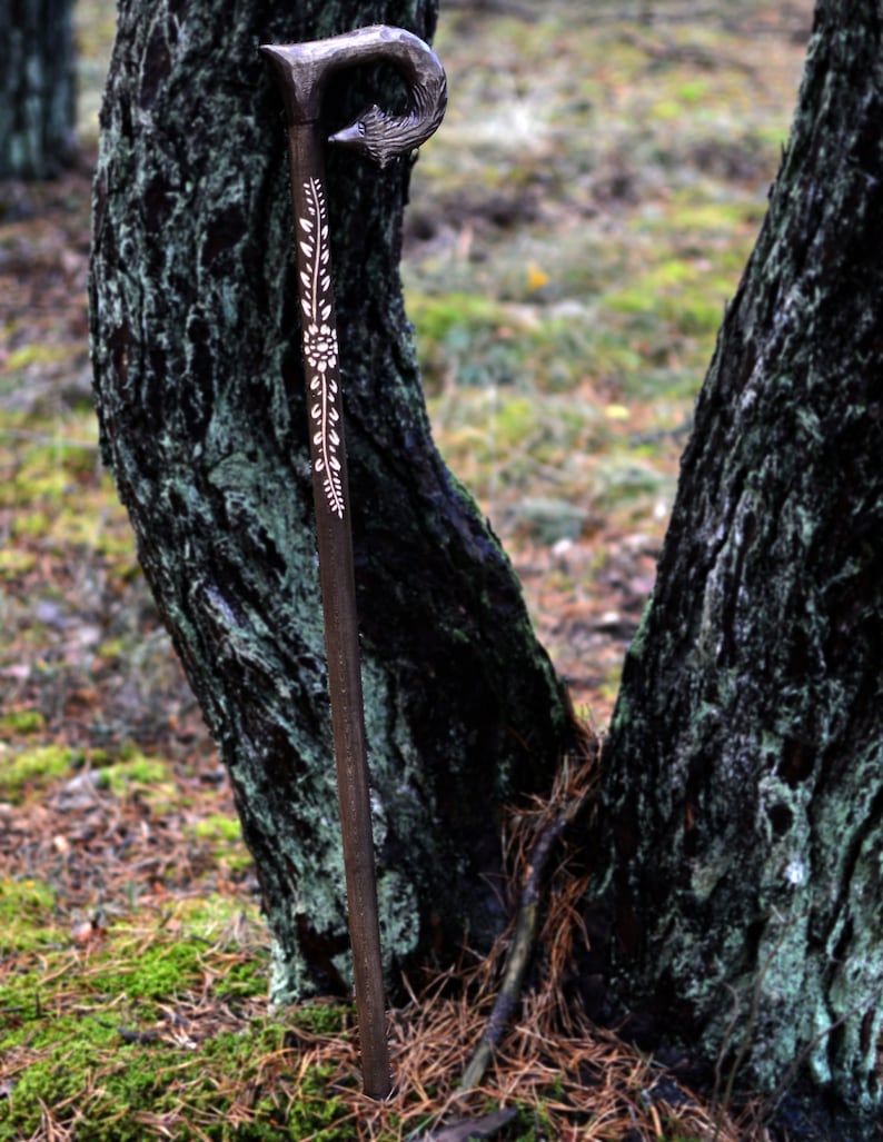 May include: A wooden walking stick with a carved, curved handle and a floral design. The stick is brown and the design is white.