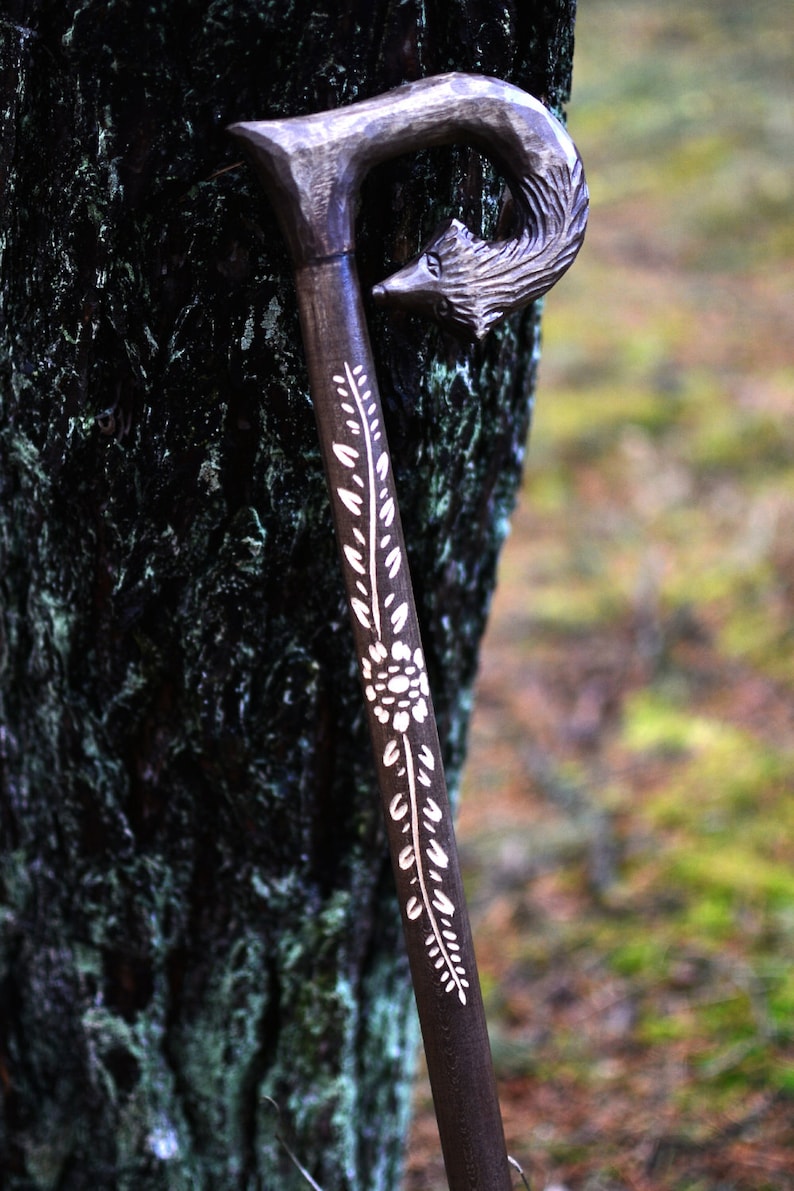 May include: A wooden walking stick with a carved wolf head handle and a white floral design.
