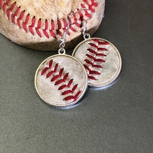 Puede incluir: Pendientes de b&eacute;isbol plateados con dise&ntilde;o de b&eacute;isbol. Los pendientes tienen un colgante circular con un dise&ntilde;o de costura de b&eacute;isbol en hilo rojo. Un bal&oacute;n de b&eacute;isbol est&aacute; en el fondo. Para los fan&aacute;ticos del deporte.