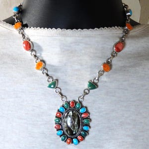 May include: A silver chain necklace with a large oval pendant featuring a black and white stone surrounded by turquoise, green, and orange stones.