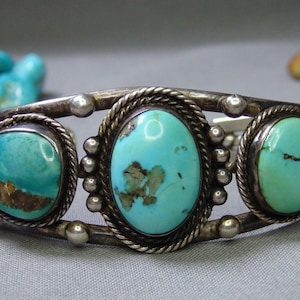 May include: Silver cuff bracelet featuring three oval and triangular turquoise stones. The turquoise stones are set in a silver frame with a twisted rope design and small silver beads. A classic Southwestern style.