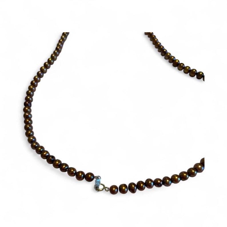 May include: A necklace composed of small, dark brown beads. The beads are strung together, forming a continuous strand. A silver-colored clasp secures the necklace. The necklace is displayed against a white background.