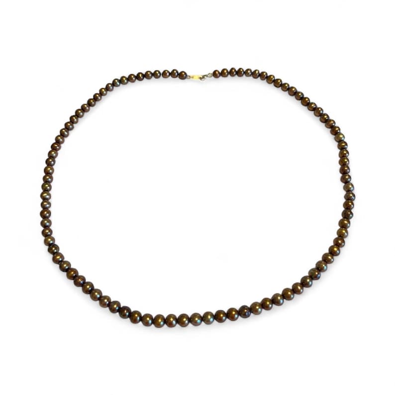 May include: A dark brown beaded necklace with a gold clasp. The necklace is composed of small, round beads, evenly spaced along the strand. The beads have a subtle sheen, reflecting light. The necklace is displayed against a white background.