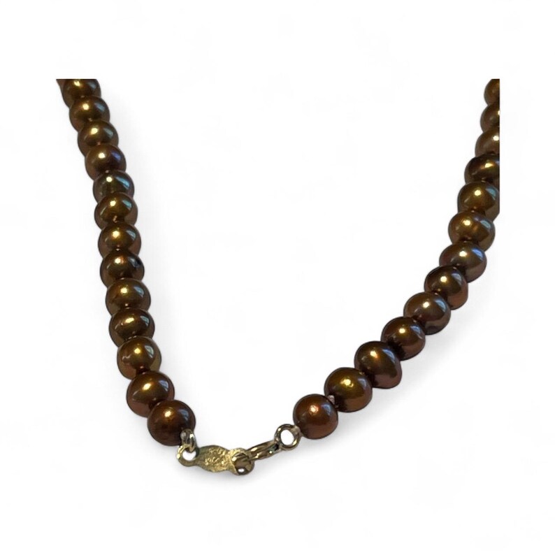 May include: A necklace featuring lustrous, dark brown pearls. The pearls are strung together, creating a continuous strand. The necklace is secured with a gold-colored clasp.