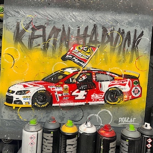 May include: A vibrant artwork featuring a red and white race car with the number 4, sponsored by Budweiser. The car is set against a yellow and gray background, with the name "KEVIN HARVICK" in graffiti style. A checkered flag waves above the car.