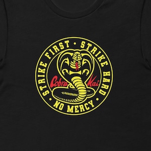 May include: Black t-shirt with a yellow circle graphic featuring a cobra with red eyes and the text "Strike First Strike Hard Cobra Kai No Mercy".