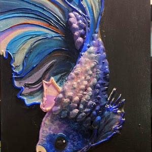 May include: A textured painting of a betta fish on a black canvas. The artwork uses shades of blue, purple, and pink, with detailed brushstrokes creating a three-dimensional effect. The fish's flowing fins and scales are the focal point of the painting.