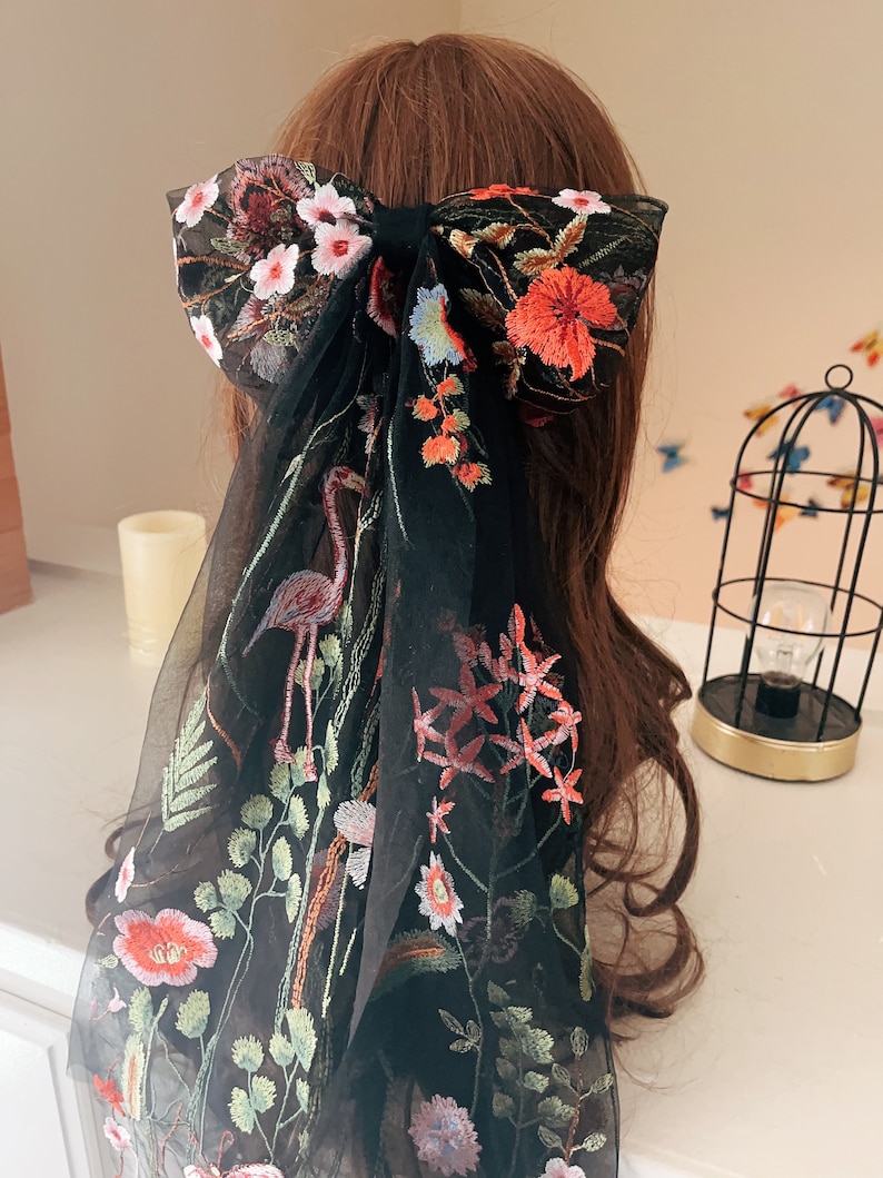 May include: Black sheer hair scarf with floral embroidery. The embroidery features pink, red, and green flowers, as well as a flamingo.