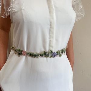 K&ouml;nnte beinhalten: Ein wei&szlig;es Kleid mit Spitzen&auml;rmeln und einem floral bestickten G&uuml;rtel.