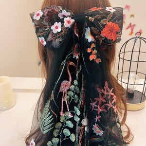 May include: Black sheer hair scarf with floral embroidery. The embroidery features pink, red, and green flowers, as well as a flamingo.