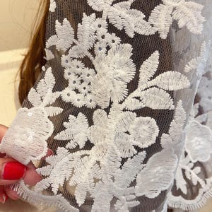 May include: White floral lace fabric with a delicate mesh background. The lace features a floral pattern with small sequins.