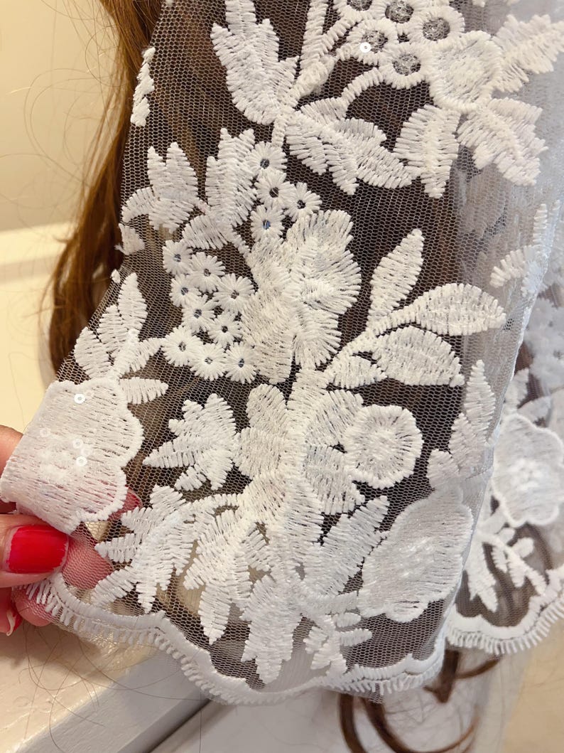 May include: White floral lace fabric with a delicate mesh background. The lace features a floral pattern with small sequins.