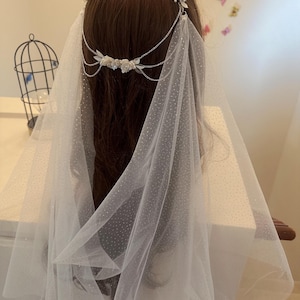 May include: White bridal veil with a delicate dot pattern and a silver chain with floral accents.
