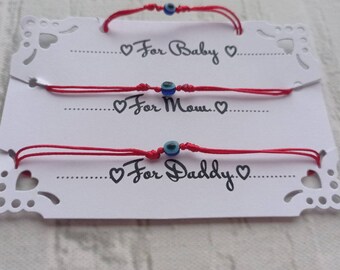 May include: Three red string bracelets with blue evil eye charms. The bracelets are labeled "For Baby", "For Mom", and "For Daddy".