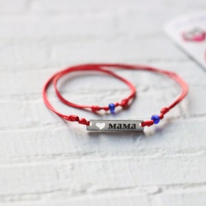May include: Two red string bracelets with blue beads and a silver charm that says "MAMA" with a heart cutout.
