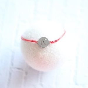 Peut inclure: Un bracelet en cordon rouge avec un charme argenté en forme de cercle avec la lettre "K".