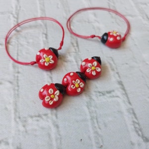 May include: Two red string bracelets with ladybug charms. Each charm has a white flower with a yellow centre.