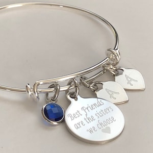 May include: Silver bangle bracelet with charms. The charms include two heart charms with the letter "A" engraved on them, a round charm with the text "Best Friends are the sisters we choose" engraved on it, and a blue crystal charm.