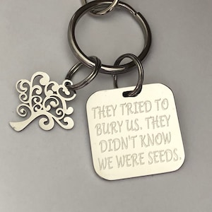 May include: Silver keychain with a tree charm and a square tag that reads "They tried to bury us. They didn't know we were seeds."